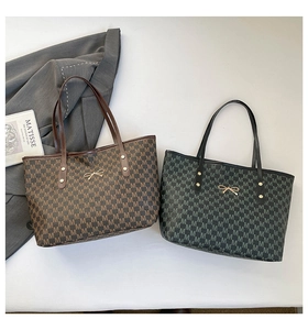 Détail de sacs fourre-tout à motif M avec boucles dorées en nœud sur un costume gris