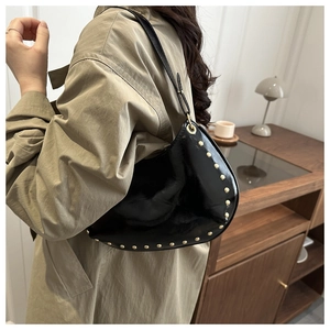 Detail of black patent leather crescent bag with gold studs worn with a trench coat