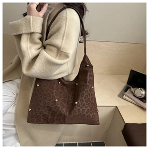 Detail of leopard print tote bag with gold studs worn by a model in an elegant winter setting
