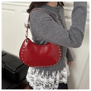 Detail of red patent leather crescent bag with gold rivets worn by a model in soft lighting