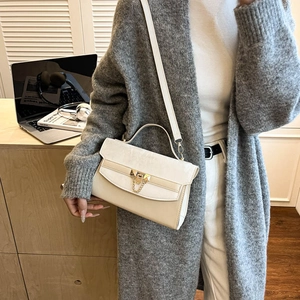 Chic beige crossbody bag with gold buckle and chain, shown in a modern desk setting