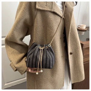 Detail of woven bucket bag with pearl drawstring accent and golden chain strap