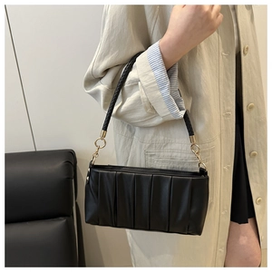 Detail of black pleated shoulder bag featuring a woven handle and gold hardware