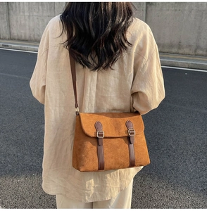 Close-up of brown suede messenger bag with vintage buckles and flap cover detail