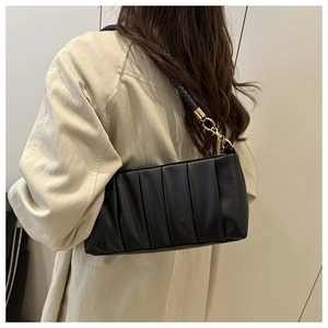 Detail of black pleated shoulder bag with woven strap shown on a model's shoulder