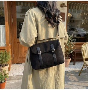 Close-up of a large black messenger bag with leather straps on a model in a cafe setting