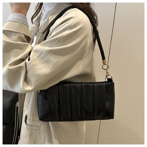 Detail of black pleated shoulder bag featuring unique woven strap and gold hardware