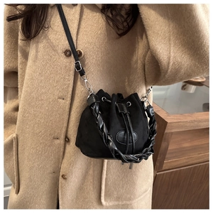 Detail of a black suede bucket bag with woven handle and drawstring closure