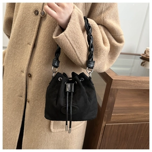Detail of black suede-textured bucket bag with woven handle and drawstring closure