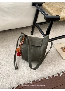Detail of dark green bucket bag with white stitching and decorative charm on white rug
