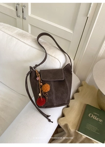 Detail of dark brown matte bucket bag featuring white stitching and colorful fur pompom