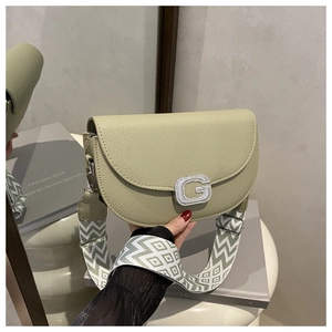 Close-up of sage green litchi leather saddle bag with rhinestone G-buckle and woven strap