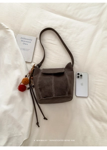 Detail of a dark brown bucket bag with white stitching and colorful tassel decor