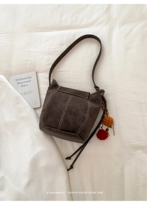 Detailed close-up of dark brown suede shoulder bag with contrast stitching and pom-pom charm