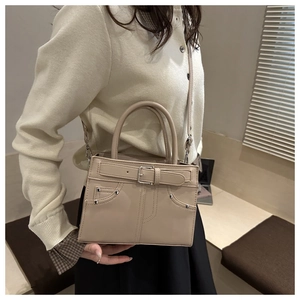 Detail of beige tote bag featuring decorative pockets, metal buckles and silver rivets