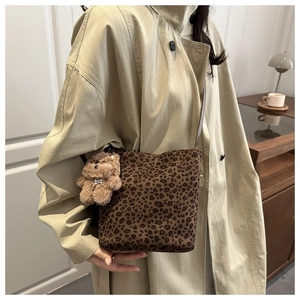 Detail of leopard print suede crossbody bag with bear charm on a trench coat