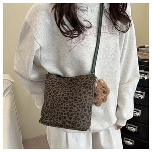 Detail of leopard print crossbody bag with green leather strap and teddy bear charm