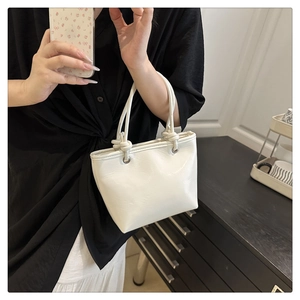 Detail of white PU leather tote bag featuring a unique knotted handle and metallic hardware