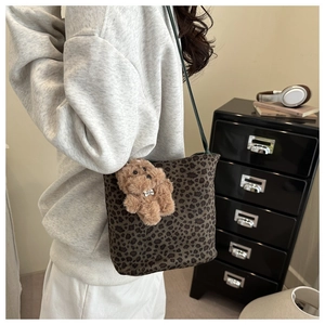 Detail of leopard print bucket bag with brown plush bear charm and green strap