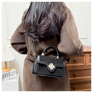 Detail of elegant black matte shoulder bag with golden rose-shaped buckle and twisted handle