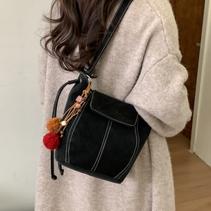 Minimalist black suede bucket bag with white contrast stitching and tassel charm