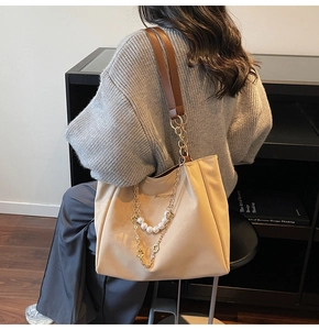 Detail of beige tote bag with wide brown strap and decorative pearl chain accent