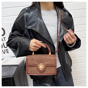 Detail of a brown suede flap handbag featuring a golden clover lock and twisted ring handle