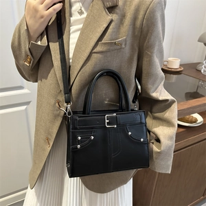 Minimalist black leather crossbody bag with silver studs and buckles in cafe setting