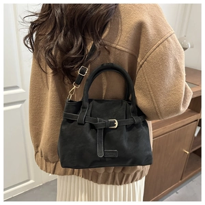 Rear view of model wearing a black suede crossbody bag with belt buckle detail