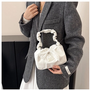 Pleated white satin handbag with a large bow and chain strap on a blazer