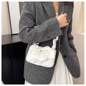Detail of white bow handbag with ruched handle on a model wearing tweed blazer