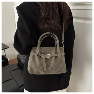 Detail view of suede commute handbag with gold buckle and adjustable strap on a model
