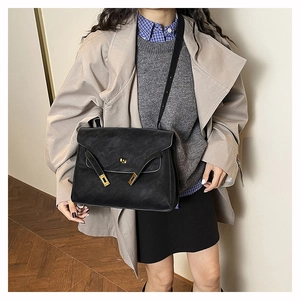 Detail of a black leather crossbody bag with golden hardware lock shown on a model