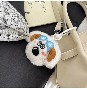 Détail d'un charme chiot en peluche blanche avec lunettes bleues sur un sac à main