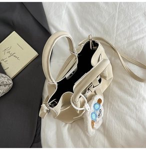 Détail d'un sac à main crème avec pendentif en peluche et fermoir magnétique chic
