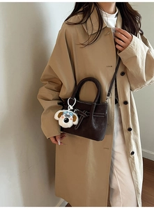 Détail du sac à main en cuir mat marron foncé avec surpiqûres et breloque chien peluche