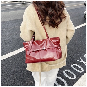 Détail du sac à bandoulière en cuir verni bordeaux brillant sur un manteau beige