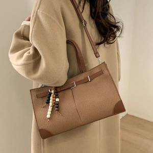 Brown woven tote bag with buckle detail and beaded tassel, styled on model in camel coat