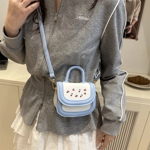 Mini sky blue and white crossbody bag with cherry prints and top handle on a model