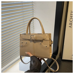 Detail of beige faux leather handbag with decorative buckle and silver rivets shown in hand
