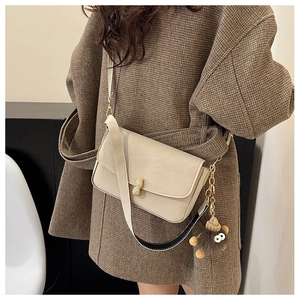 Detail of beige leather crossbody bag featuring gold peanut buckle and plush pendant charm