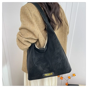 Minimalist black leather tote bag with yellow JACQUEUE logo worn by a model in a beige suit
