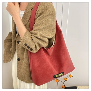 Model wearing a red leather tote bag styled with a plaid blazer and long white skirt