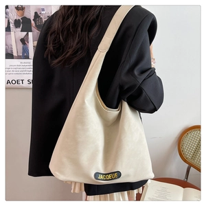 Close-up of the beige leather tote bag featuring a black JACQEUE logo label at the base