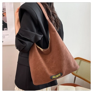 Detail of a dark brown suede tote bag featuring a leather logo patch and wide strap