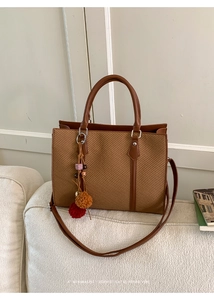 Detail of a brown woven tote bag featuring a leather strap and decorative bag charm