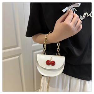 Detail of a white mini crossbody bag with a 3D red cherry and golden chain strap