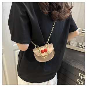 Detail of beige mini saddle bag with red cherry accents and chunky gold chain strap