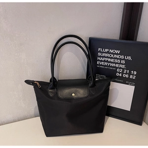 Detail of black nylon tote bag featuring leather flap and gold metal buckle closure