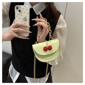 Detail of light green mini bag featuring crystal cherry decor and gold chain strap
